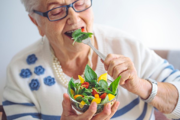 A senior woman eats a leafy salad, which is good for brain health.