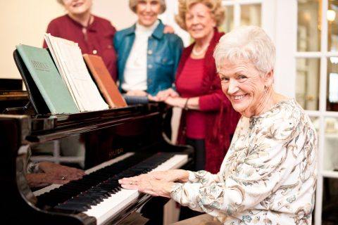 A senior woman playing the piano for 3 other seniors