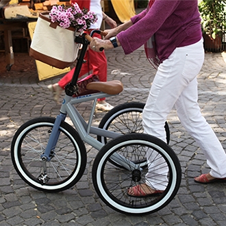 A woman walking outside with a tricycle, with a basket with flowers in it.