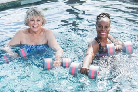 Two senior women use water weights to work out in a pool.