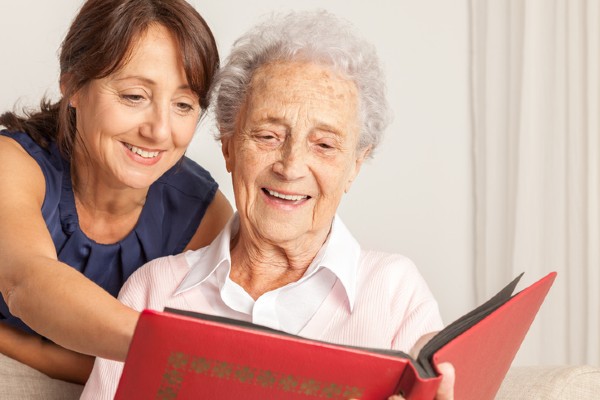 A senior woman and her caregiver rekindle memories by looking through a photo album.