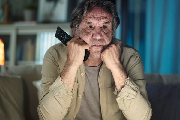 A senior man passes the time on his couch, intently watching television.