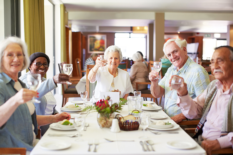 A group of seniors raising their glasses during a meal at a senior living community.