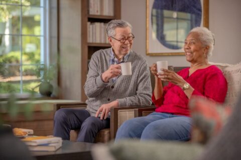 Two seniors sitting together drinking coffee at their senior living community.