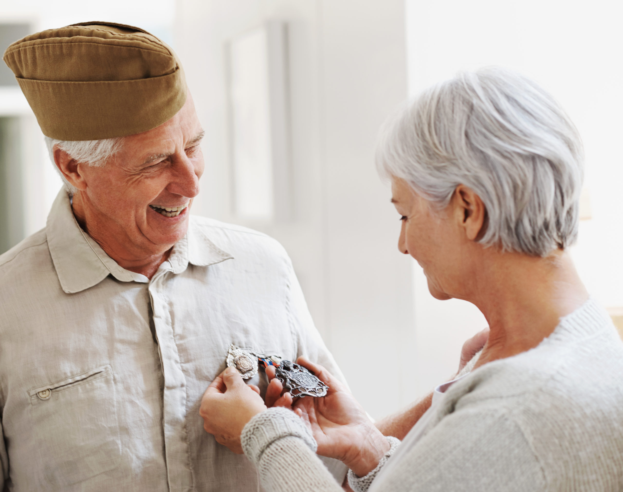 A senior woman looking at her husband's medals as he stands wearing his military uniform