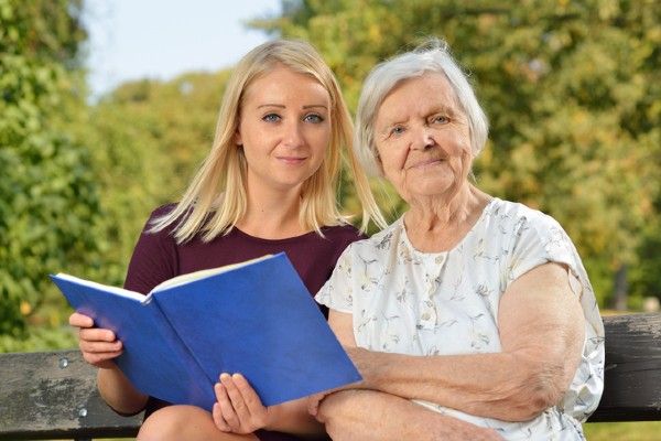 A woman shares a book with an elderly person in her care.