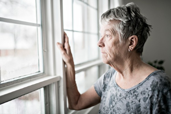 A depressed senior woman stares out her window.