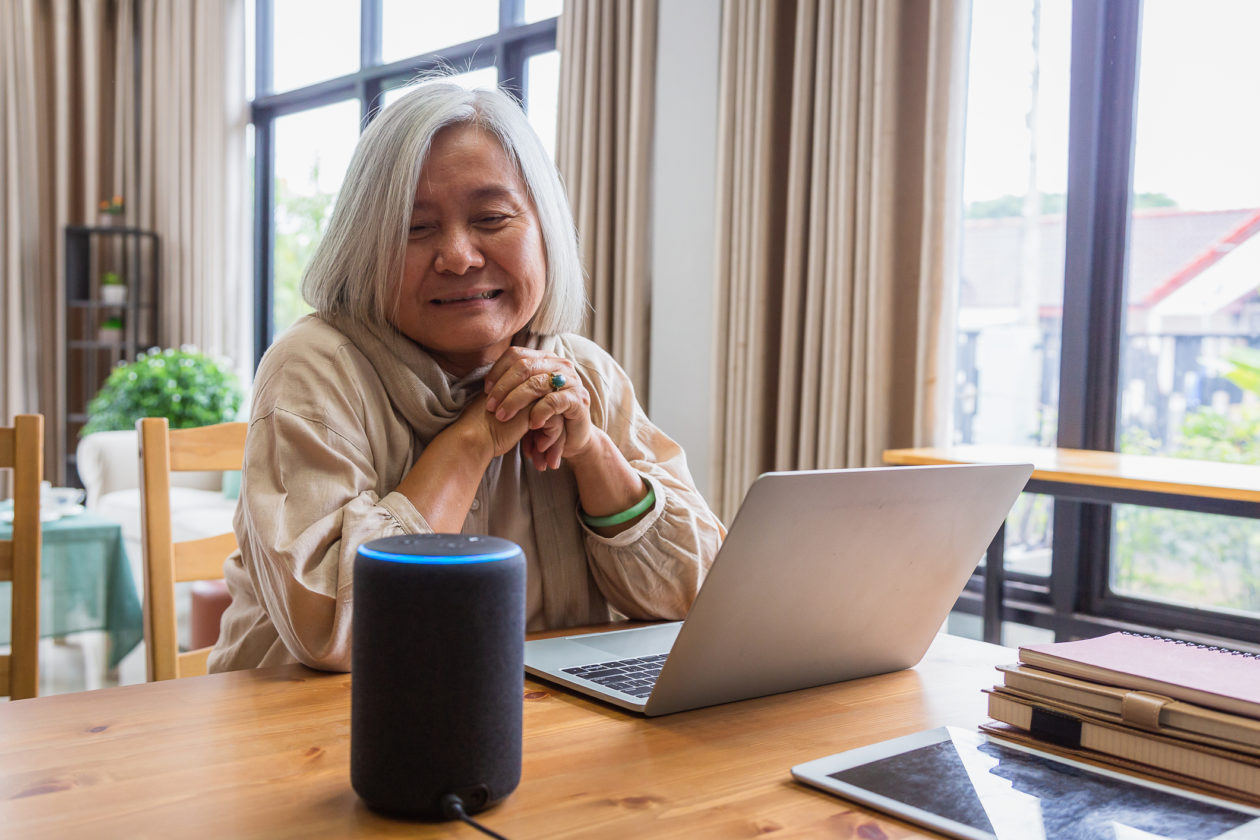 Asian senior women working with laptop computer and using smart speakers while setting in living room at home