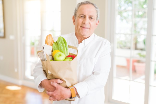 A healthy senior man carries a bag full of groceries.
