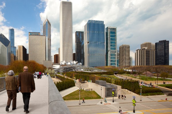 A senior couple crosses the Nichols Bridgeway at Millennium Park with the Chicago city skyline in the background.