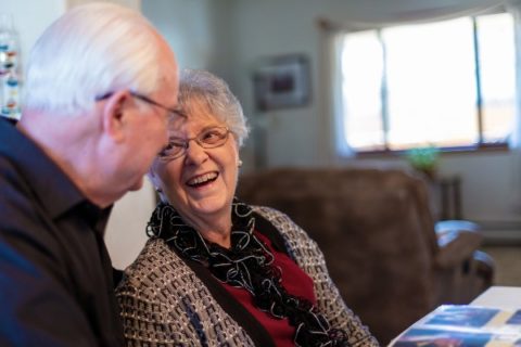 A senior man helps his wife rekindle memories with a photo album.