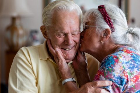 A senior woman kisses her husband who is living with dementia.