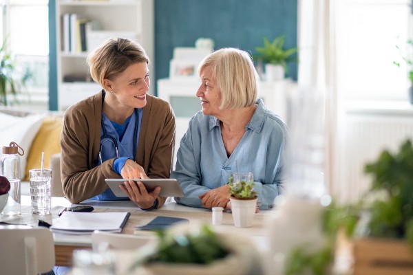 A caregiver helps a senior woman on a computer tablet.