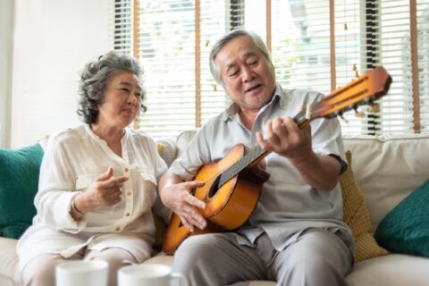 An older man plays guitar as his partner sings along.
