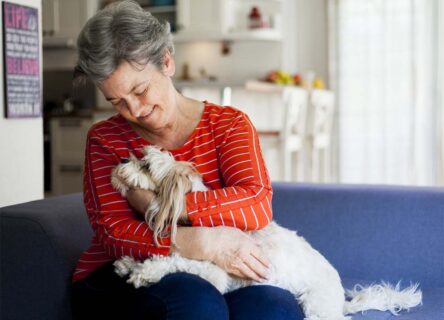 Elderly woman petting a dog in her lap.