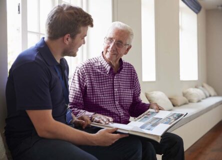 Elderly man looking at book with friendly nurse