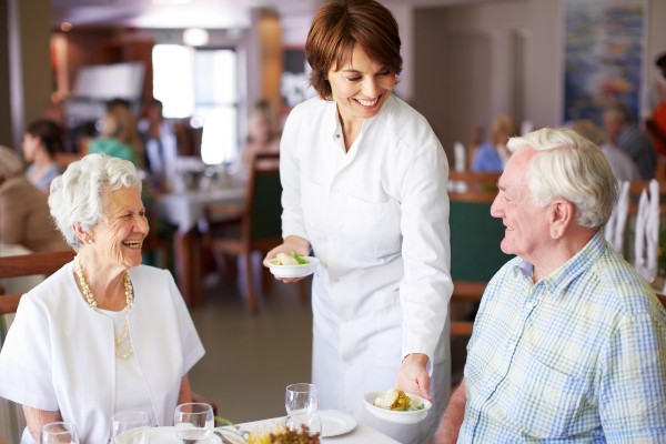 A hostess serves two seniors at a care community. Seniors face more food allergies as they age.