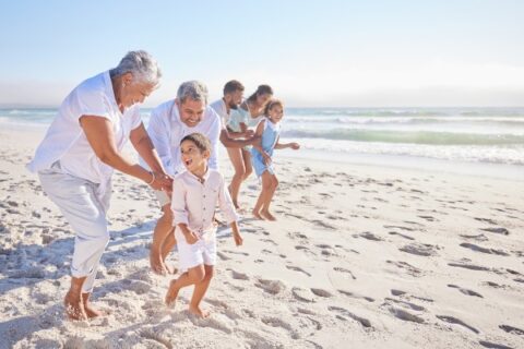 An active senior couple visits the beach with their grandchildren and children.