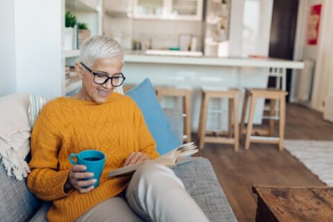 An older woman in assisted living enjoys coffee and a book.