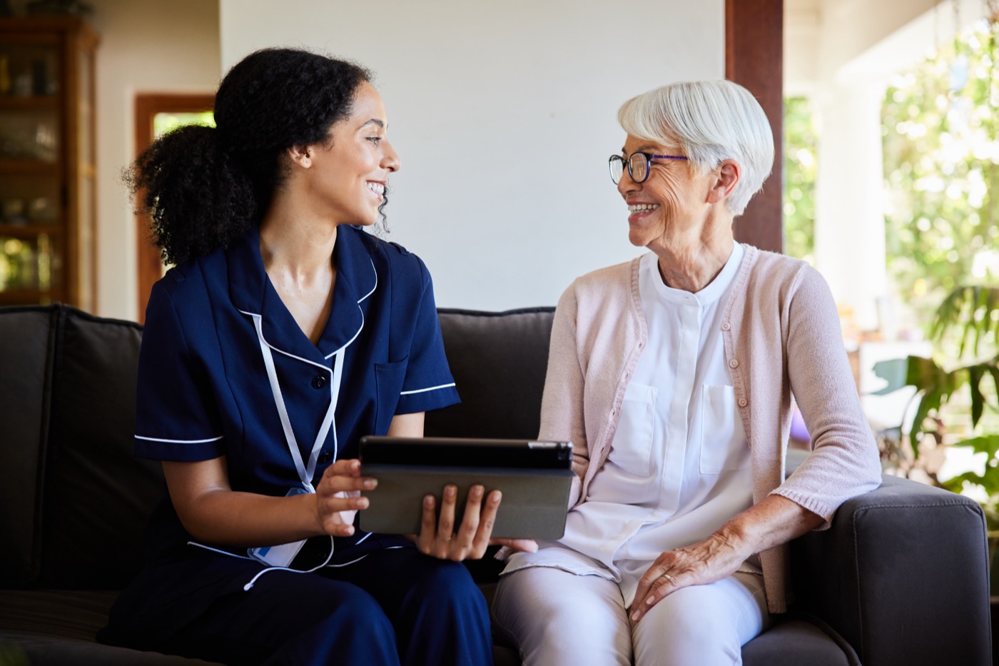 Senior woman and a home healthcare worker laughing while using a tablet