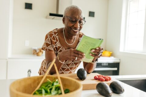 A senior woman in a kitchen reads a recipe for a healthy snack.