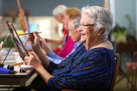 A senior woman smiles while working on her painting during a class at a senior living community.
