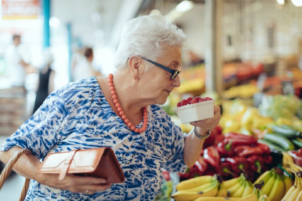 A senior woman checks a basket of berries while grocery shopping.