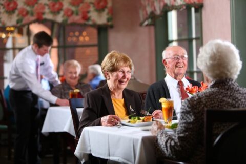 A group of seniors enjoy restaurant-style dining with a server nearby.