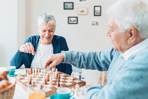 A senior couple playing chess and smiling at a senior living community.