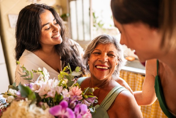 Two daughters honor their senior mother with flowers at home.