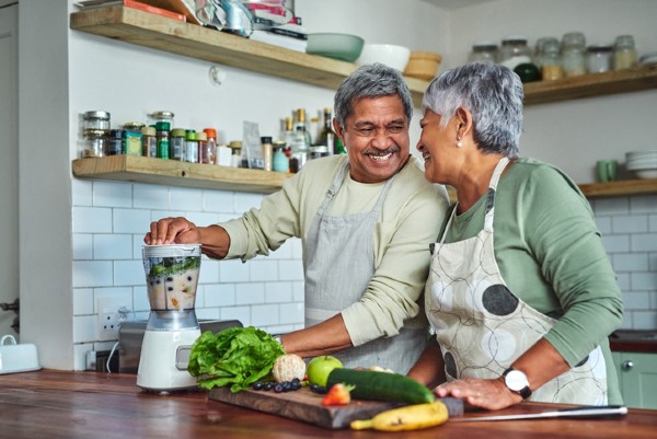 A senior couple preparing a healthy smoothie in the kitchen at home.