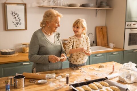 Granddaughter helping grandmother make holiday cookies in the kitchen.