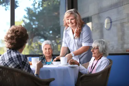 staff member helping senior residents at dining table