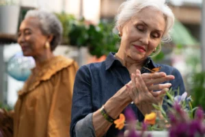 A senior woman holds a monarch butterfly in her hand in a greenhouse