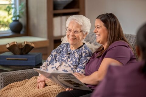 A senior and her caretaker share a book.