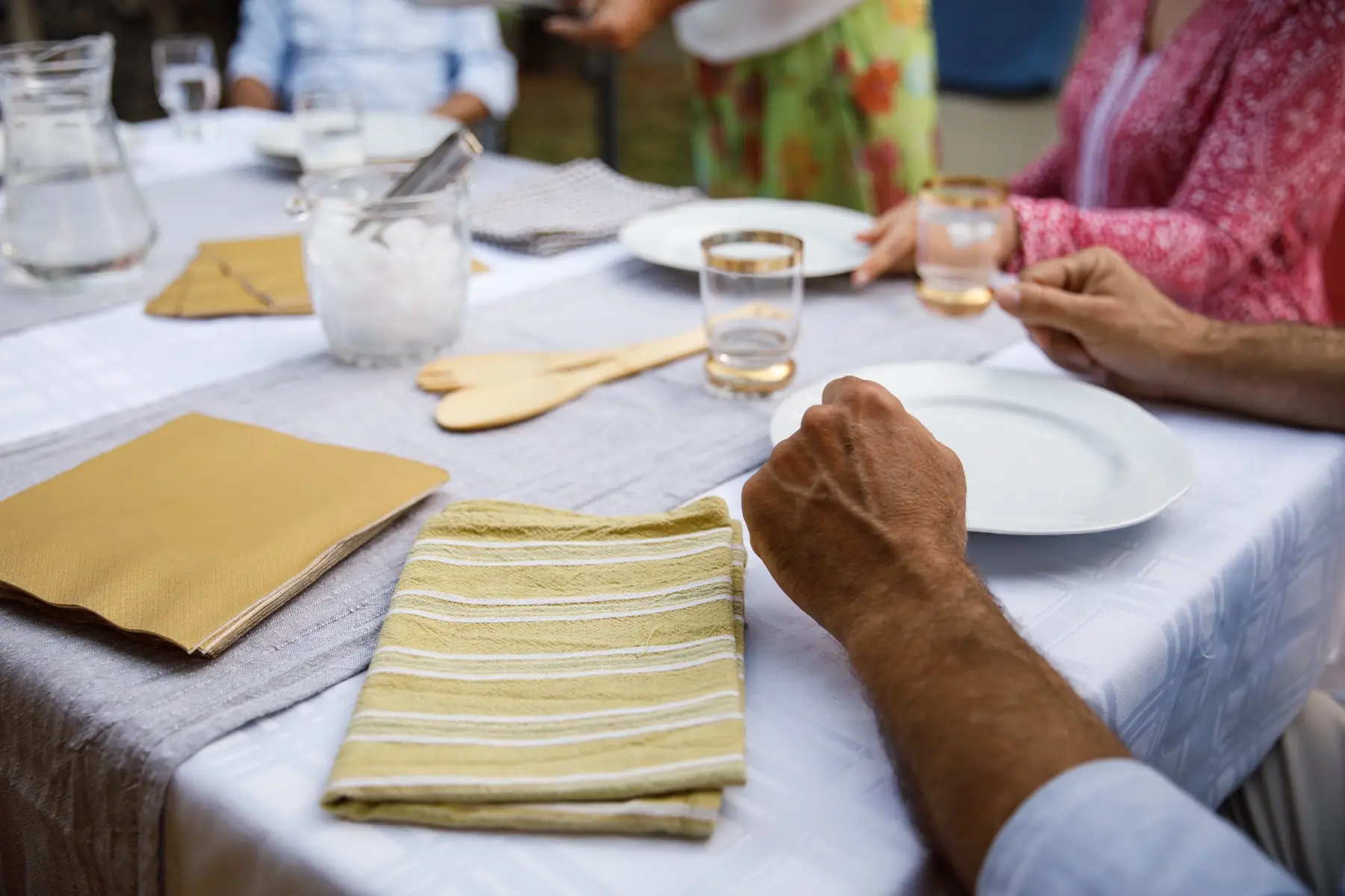 Man sitting at table, waiting for food during a dinner party at his friend’s Close up shot of unrecognizable man sitting at the top of a dining table, resting his hands by his plate, waiting for food during a dinner party at his friend's.