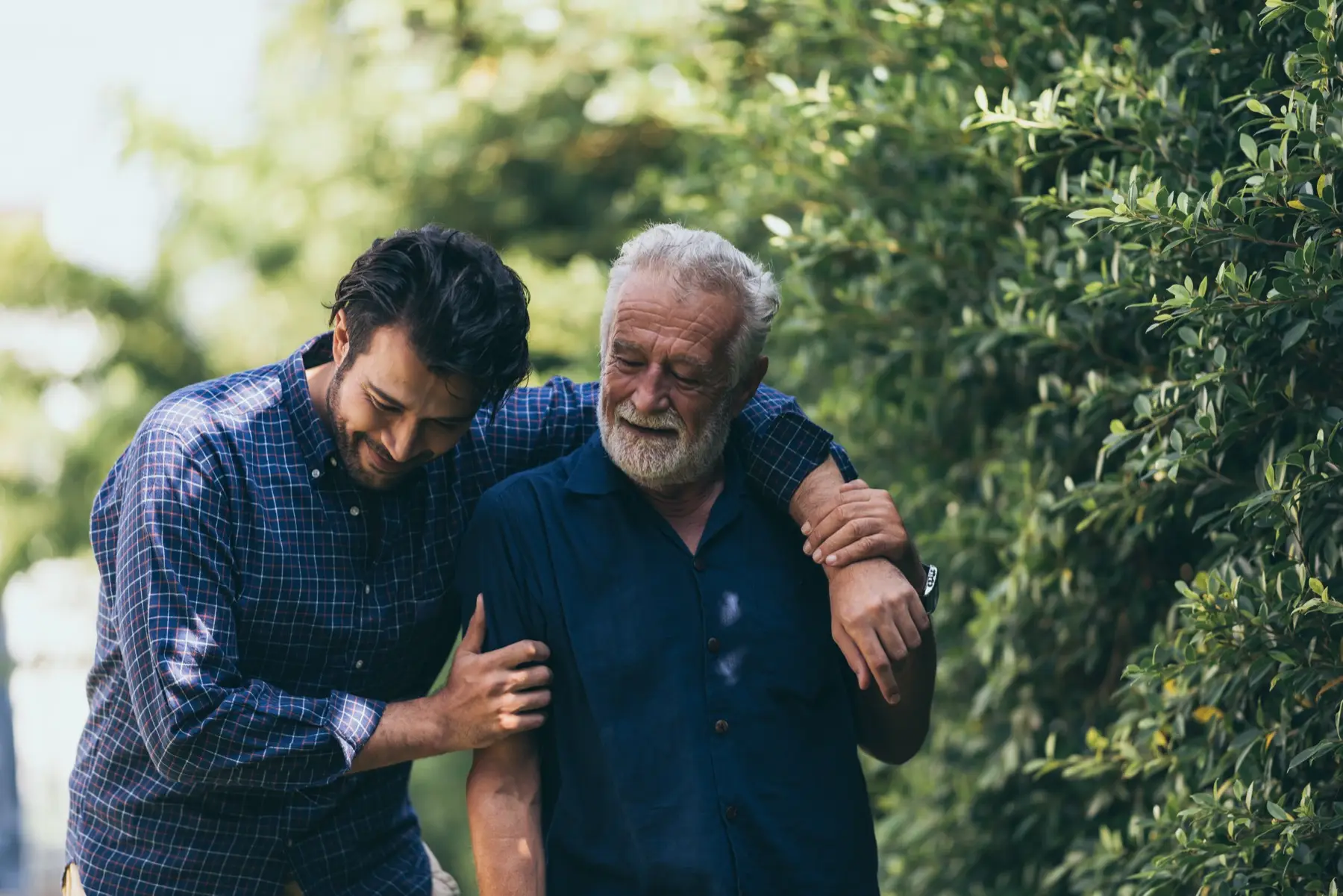 The old man and his son are walking in the park. A man hugs his elderly father. They are happy and smiling The old man and his son are walking in the park. A man hugs his elderly father. They are happy and smiling