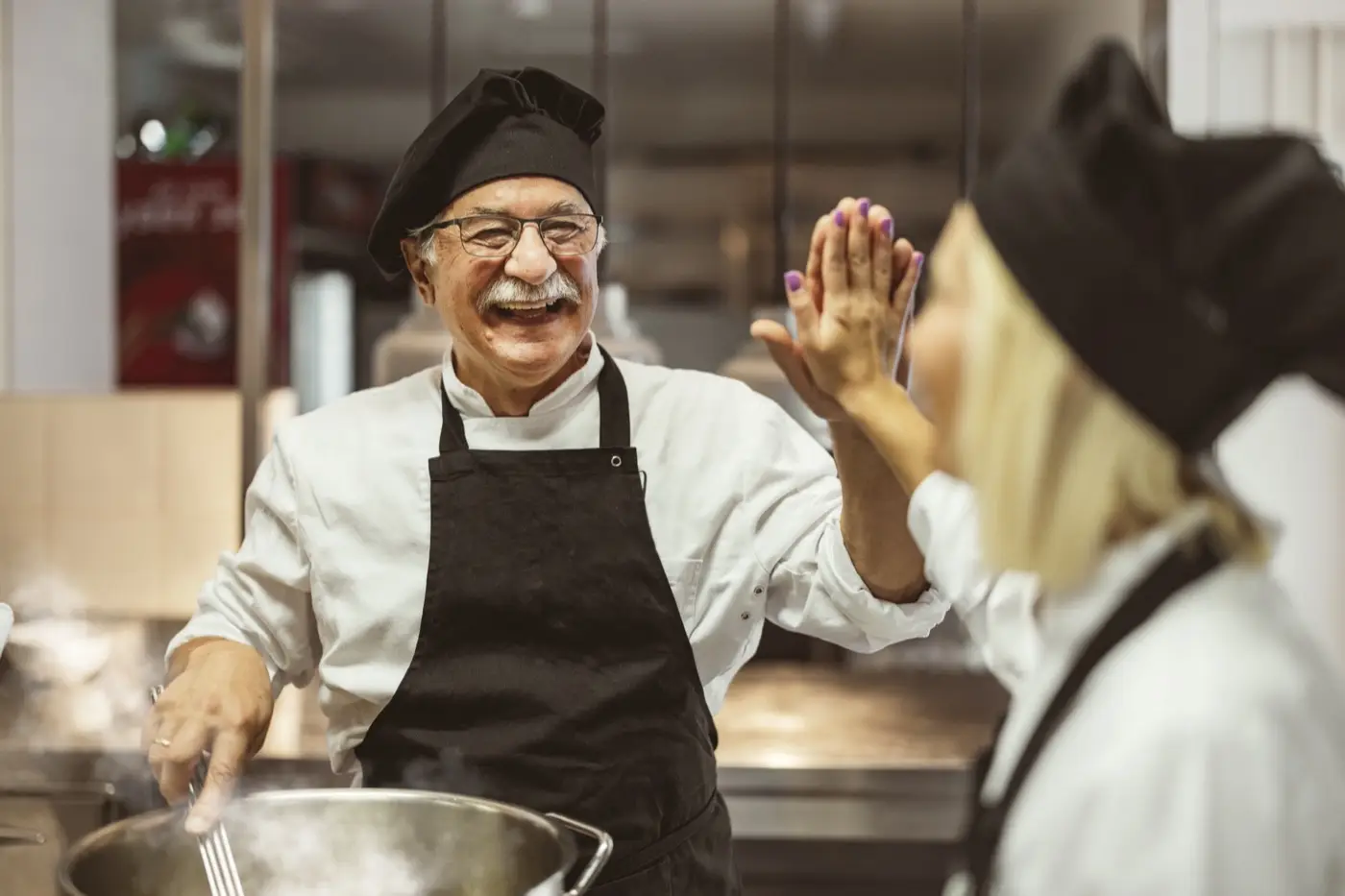 We made it! Team of cooks giving five with hands each other, while cooking in professional kitchen. Concept of teamwork and success at restaurant business