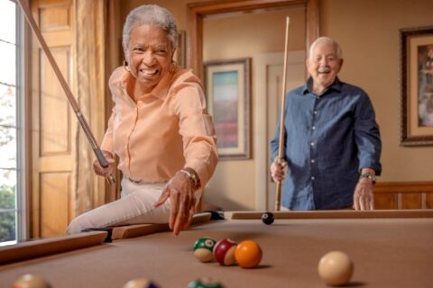 Two residents play billiards at an independent living community.