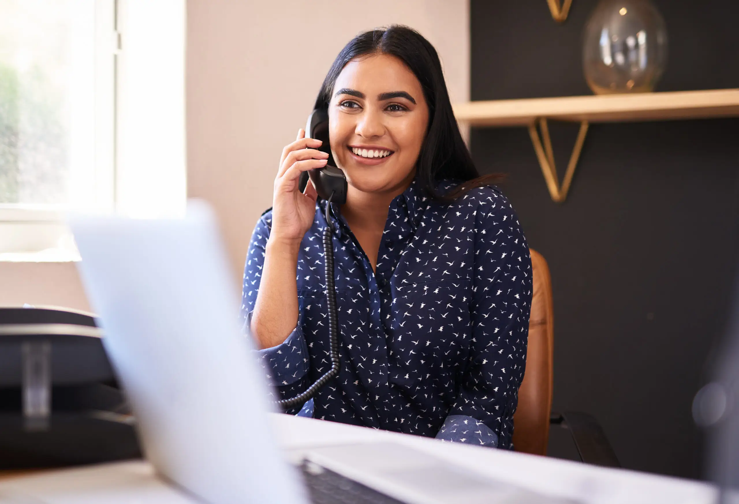 Young indian businesswoman talking on a telephone in an office alone. One female only making a call while working as a receptionist at a front desk. Administrator and secretary consulting and transferring calls from a help desk in a call centre Administrative employee at senior lifestyle answering phone call