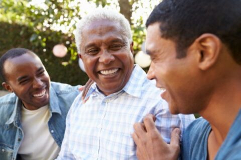 Senior man smiling and laughing with his sons during an outdoor family gathering.