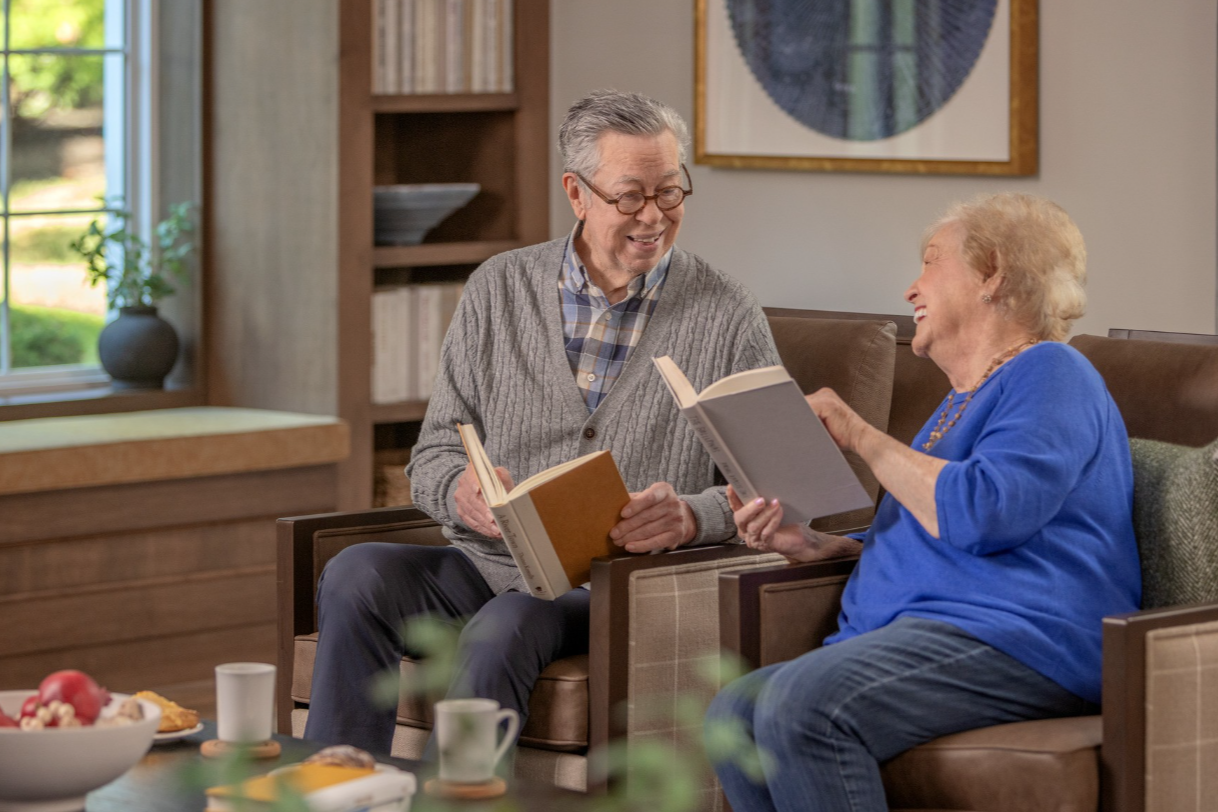 Two Senior Lifestyle residents read books together in a community setting.