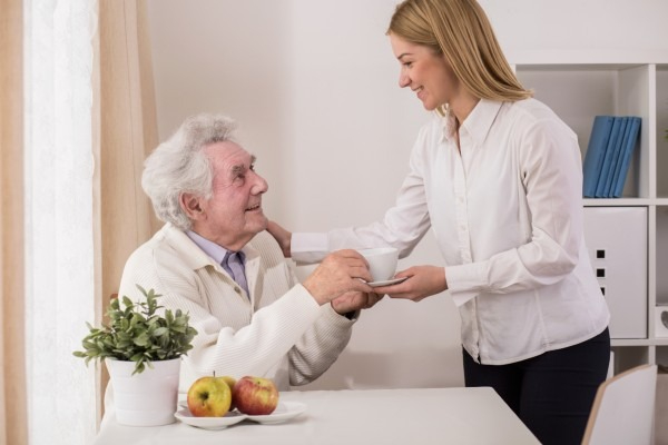 A senior in memory care is handed a drink.